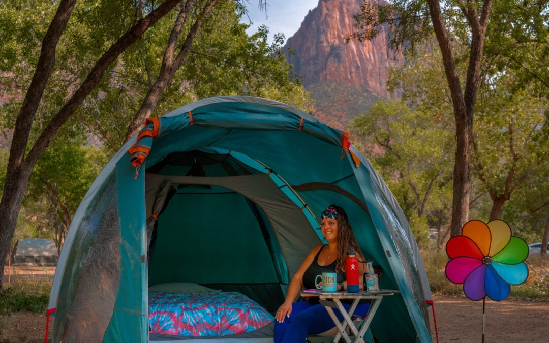 female sitting in tent with her car camping gear while car camping under the mountains of Zion National Park